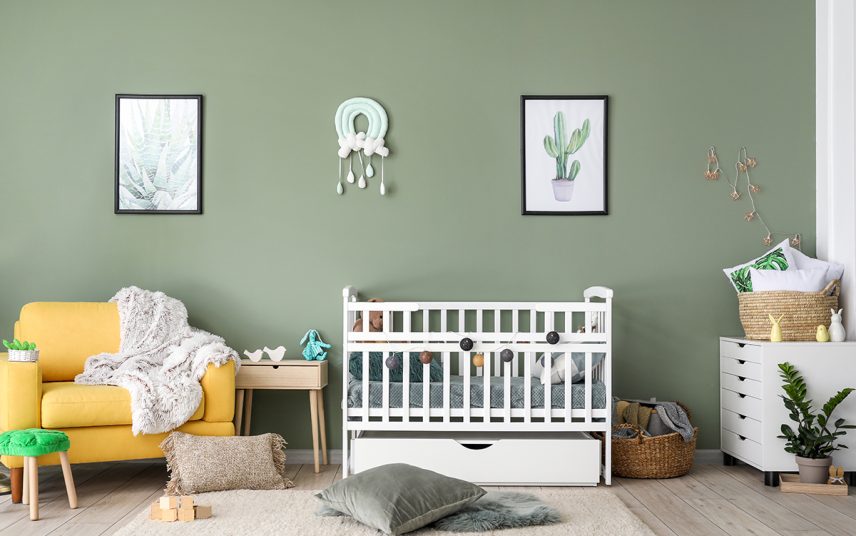 Gestaltungsidee für ein gemütliches Babyzimmer mit grüner Wandfarbe – weißes Babybett & Beistelltisch aus Holz – gelber Sessel & weiße Kommode
