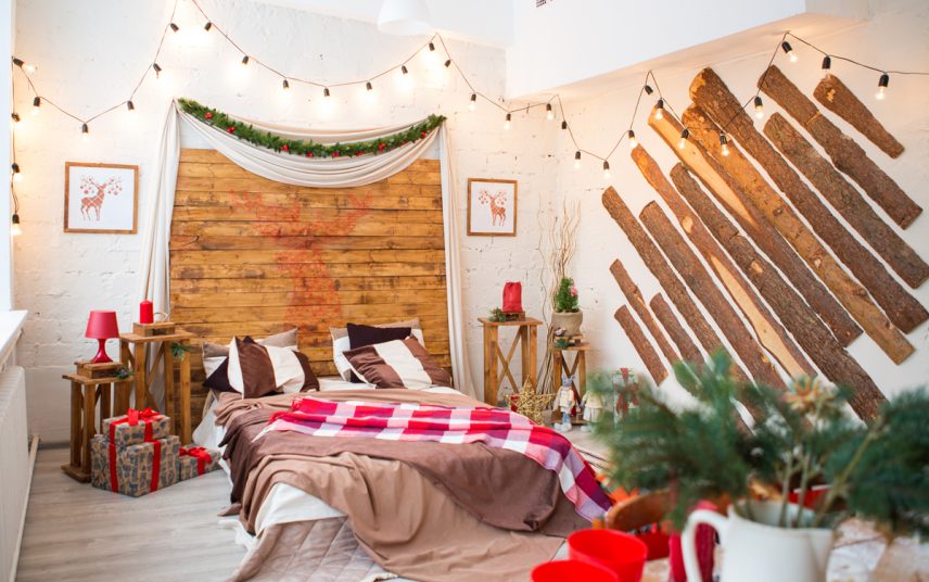 Wohnidee – Jugendzimmer für Jungs mit weihnachtlicher Dekoration – Großes Doppelbett mit vielen Decken & Beistelltische – stilvolle Holzverkleidung an den Wänden – Lichterkette für schönes Lichtambiente