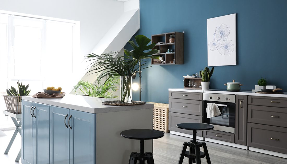Gemütliche moderne Küche in Blau mit Deko - Beispiel mit Kücheinrichtung & Barhockern an der Kücheninsel Vase mit Pflanzen - dekoriertes Wandregal