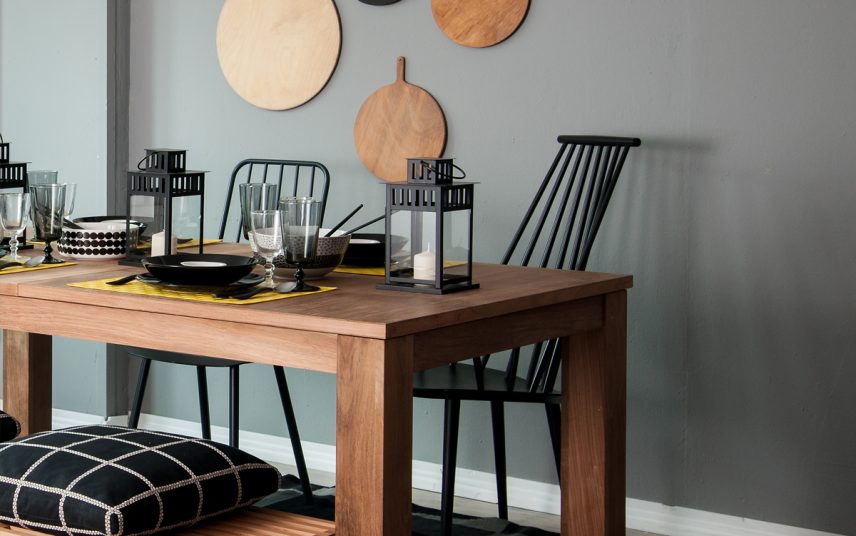 Skandinavische Küchentisch-Deko Idee – Beispiel mit einem dekorierten Holztisch mit gelben Tischset & Holzstühle – schwarze Laternen & Sitzkissen