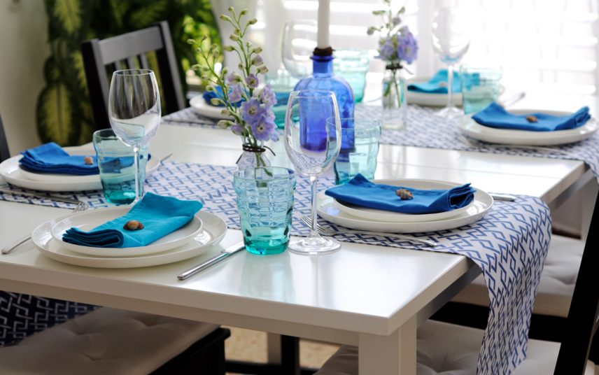 Mediterrane Tischdekoration in blau – Idee mit blauen Servietten & Tischläufer auf dem weißen Tisch – blaue Glasvasen mit Kerzen und Blumensträußen
