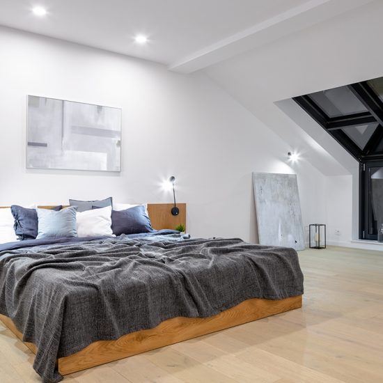 Einrichtungsidee für ein Dach Schlafzimmer - Beispiel mit modernen Holzbett mit integrierten Nachttischen & Klemmleuchten - viele Kissen
