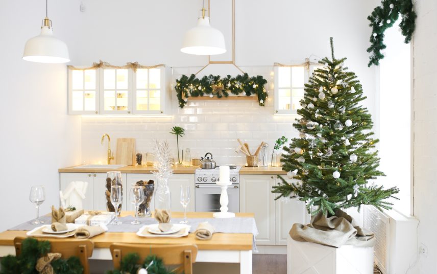 Wohnidee – Weihnachtlich dekorierte Landhausküche mit weißer Kücheneinrichtung – Beispiel mit gedecktem Esstisch  Tischläufer  Kerzenständer & Glasvase – Lichterketten & Weihnachtliche Dekokugeln