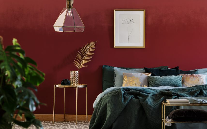 Deko Idee für ein elegantes Schlafzimmer – Weinrote Wandfarbe mit Wanddekoration – Großes Bett – Beistelltisch aus Metall mit Dekovase & Dekofigur – Moderne Hängelampe