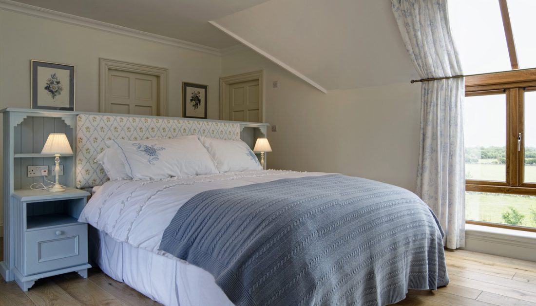 Gestaltungsidee für ein Landhaus Schlafzimmer in der Ferienwohnung - Beispiel mit großen Landhausbett mit integrierten Nachtschränken - weiße Nachttischlampen - Bilderrahmen als Dekoration