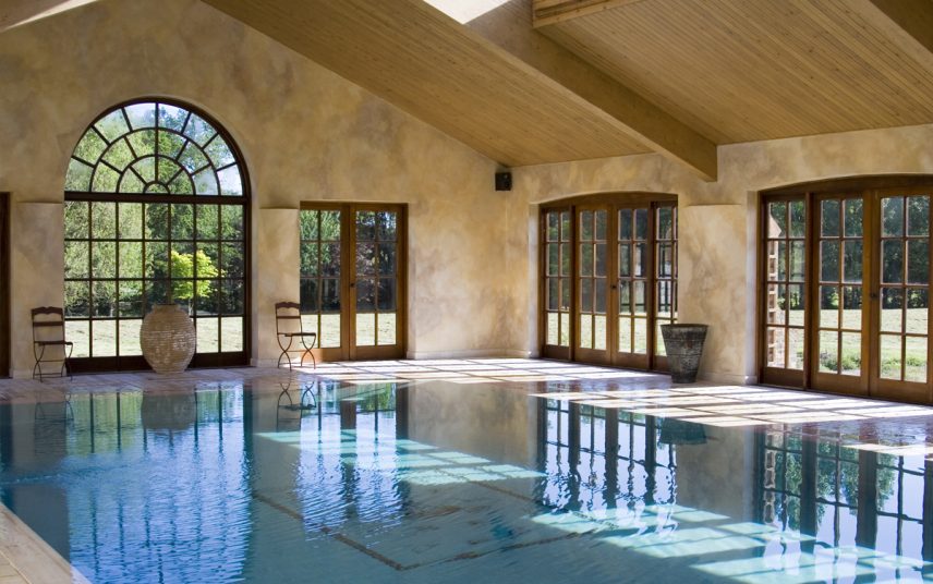 Luxus Poolhaus Idee im mediterranen Stil mit Dachschrägen – Einbaupool mit blauen Fliesen – Stühle aus Schmiedeeisen & große Vasen am Poolrand