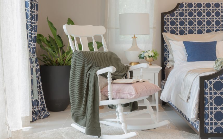 Landhaus Schlafzimmer Deko Idee mit weißen Schaukelstuhl – Beispiel mit dekorierten Nachttisch  Nachttischlampe & gemütliches Polsterbett – Großes Pflanzgefäß mit Zimmerpflanze