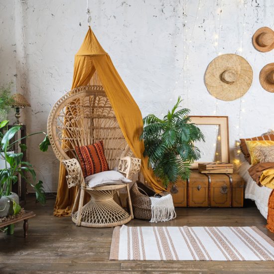Gestaltungsidee für ein Schlafzimmer im coolen Hippie Style mit Truhe als Ablage & großen Korbstuhl - Wandgestaltung mit Hüten - kleiner Teppich vor dem Bett - Zimmerpflanzen