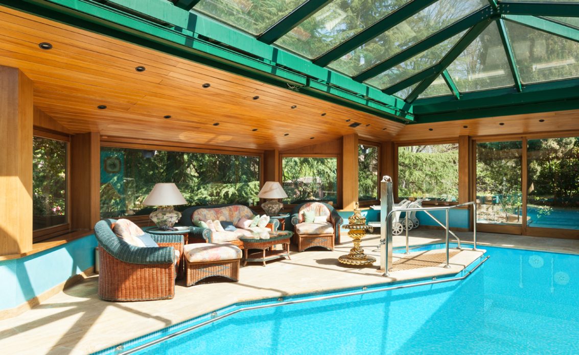 Schwimmbad Idee mit Ruhebereich unter dem schrägen Dach aus Glas & Holz – Sitzgruppe aus Rattan i...