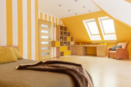 Teenagerzimmer unter dem Dach mit orangenen Akzenten – Beispiel mit Schreibtisch & Sessel unter der Dachschräge – Wandregal & Bett – Orange gestreifte Wand