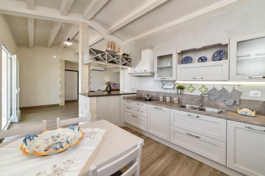 Wohnidee – Weiße Landhausküche im mediterranen Flair im Dach – Küchenzeile mit Hängeregalen – weißer Küchentisch mit weißen Stühlen