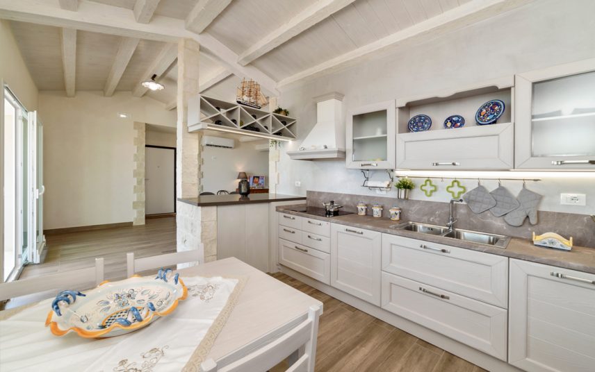 Wohnidee – Weiße Landhausküche im mediterranen Flair im Dach – Küchenzeile mit Hängeregalen – weißer Küchentisch mit weißen Stühlen