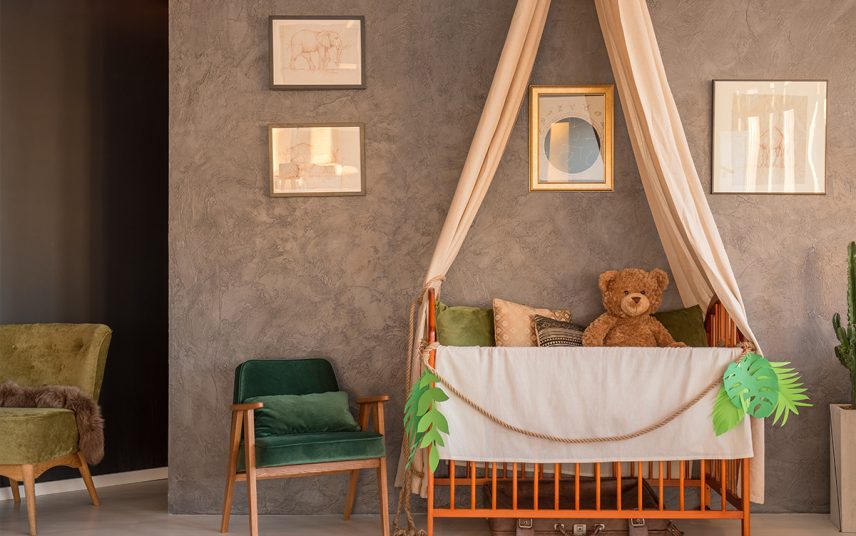 Gemütliche Babyzimmer Einrichtung mit Wandgestaltung – Beispiel mit Babybett mit Himmel & vielen Kinderkissen – Retrosessel – Bilder an der Braunen Wand mit Betonoptik
