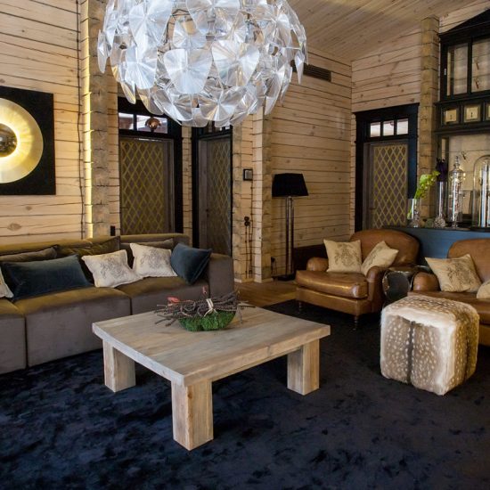 Idee für ein luxuriöses Wohnzimmer in einer Landhausvilla mit Holzvertäfelung - Beispiel mit großen Sofa & braunen Ledersesseln - Holzcouchtisch mit Gesteck - Großes Wandbild mit Beleuchtung