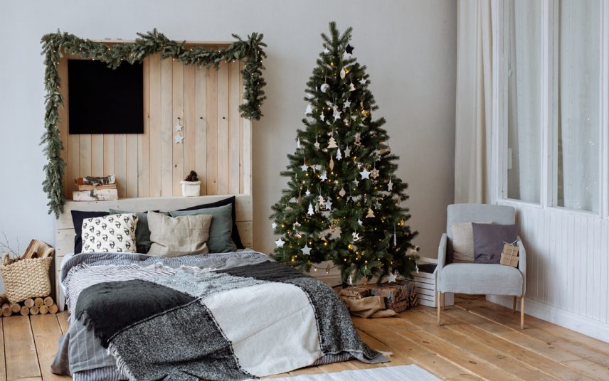 Idee für ein Schlafzimmer im Altbau mit Weihnachtdekoration – Beispiel mit Holzbett & Retrosessel – Geschmückter Weihnachtsbaum – Wandgestaltung mit Palette & Weihnachtsgirlande