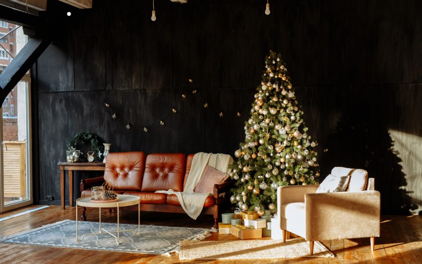 Industrieller Wohnstil kombiniert mit moderner Weihnachtsdeko – Einrichtungsidee mit Ledersofa & Retrosessel – Beistelltisch auf einem Teppich – Geschmückter Weihnachtbaum