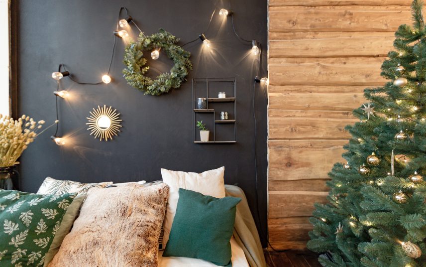 Schlafzimmer Weihnachtsdeko Idee mit Wandgestaltung – Beispeil mit Wandregal  Lichterkette & Weihnachtskranz an der schwarzen Wand – Bett mit vielen Kissen