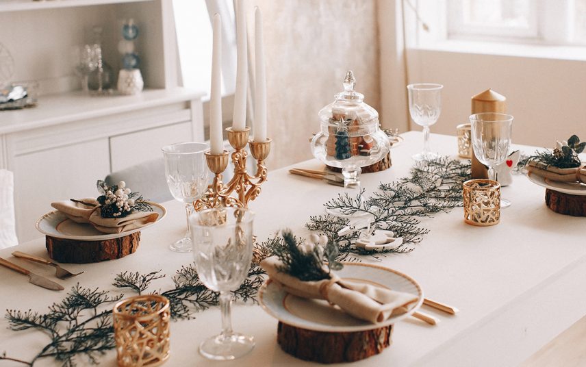 Stilvoll dekorierter Tisch mit Weihnachtsdekoration – Beispiel mit goldenen Kerzenständer  Teelichtern & Strauch auf dem Esstisch mit weißer Tischdecke