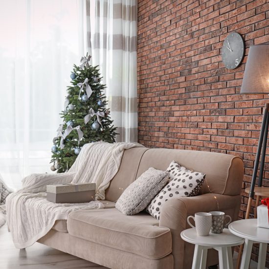Wohnzimmer im Industriellen Stil weihnachtlich geschmückt - Stoffsofa mit Kissen & Decke - Tripodlampe & weiße Satztische - Dekorierter Weihnachtsbaum mit Schleifen