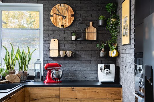Wohnidee – Rustikale Küche mit dunkler Steinwand & Wandgestaltung – schwarze Wandregale aus Metall – Küchenuhr aus Holz & Küchendekoration
