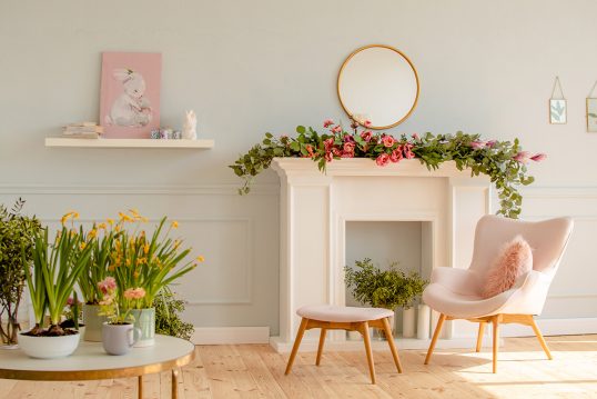 Stilvoll eingerichtete Wohnung für den Frühling – Blumengirlande auf der Kaminkonsole – Moderner Sessel mit Hocker – Wandregal mit Bild & Osterdeko