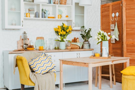 Küchen Idee mit farbenfroher Frühlingsdekoration – Gelber Blumenstrauß auf der Arbeitsfläche – Landhaus Kücheneinrichtung mit Holztisch & gelben Sessel